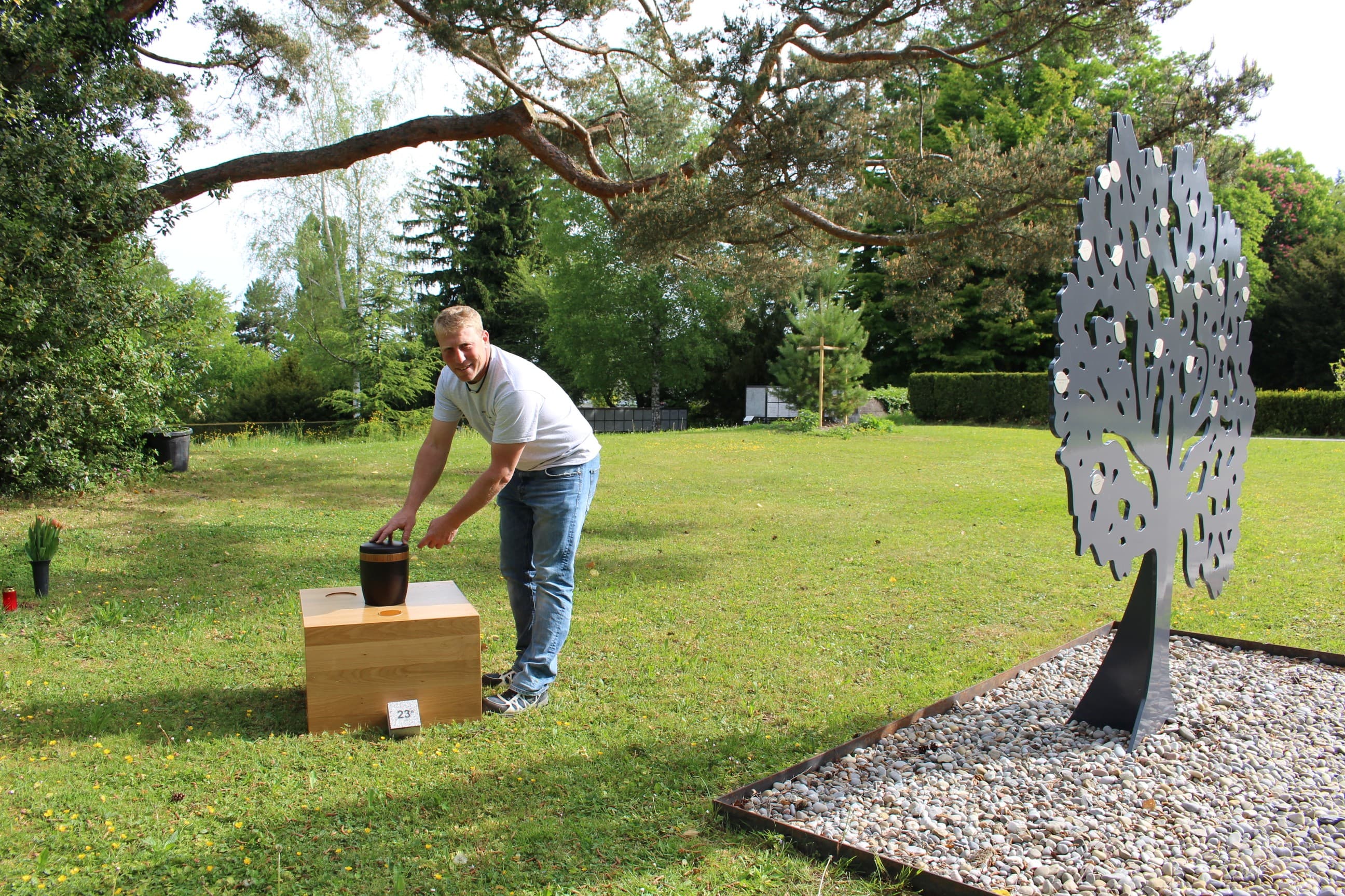 Remo Schatt, Leiter Grünanlagen der Stadt Adliswil, demonstriert, wie die Aschenbestattung vor sich geht. Im Vordergrund steht der metallene Baum mit den Täfelchen.